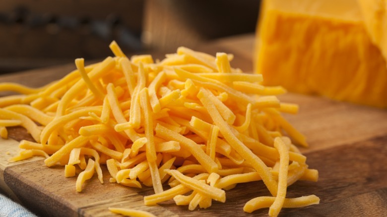 Shredded cheddar cheese on a cutting board