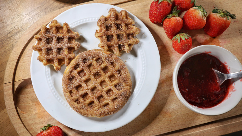 mini churro waffle Mickey Mouse face on plate with strawberries and small bowl of strawberry sauce