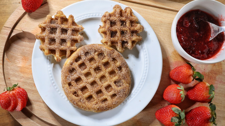 churro waffle Mickey Mouse face on white plate surrounded by strawberries and bowl of strawberry sauce