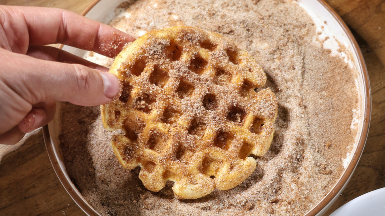 hand holding waffle coated in cinnamon sugar above plate covered in cinnamon sugar