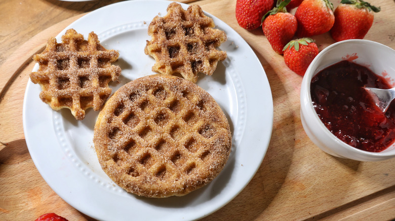 mini churro waffle Mickey Mouse face on white plate with strawberries and bowl of strawberry sauce beside it