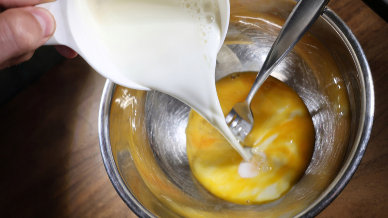 milk pouring from measuring cup into mixing bowl with fork and beaten egg in it