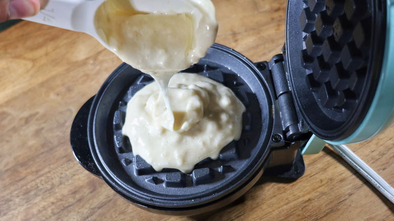 battle pouring from measuring cup into mini waffle iron