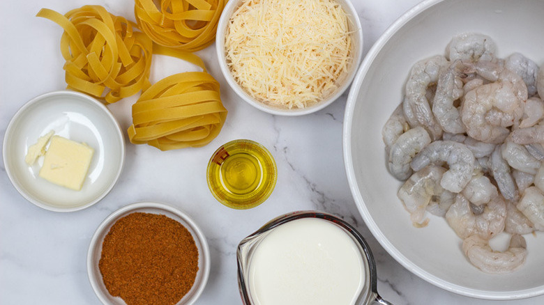 White bowls containing butter, Cajun seasoning, cream, shrimp and Parmesan