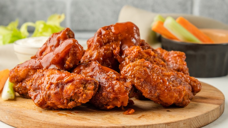 saucy buffalo wings on a wooden serving board with carrots and celery sticks