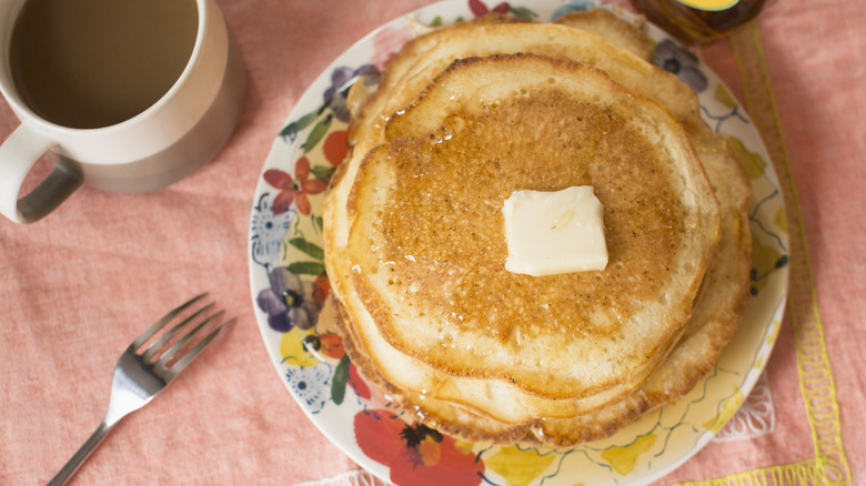 Pancakes on plate with butter and a cup of coffee