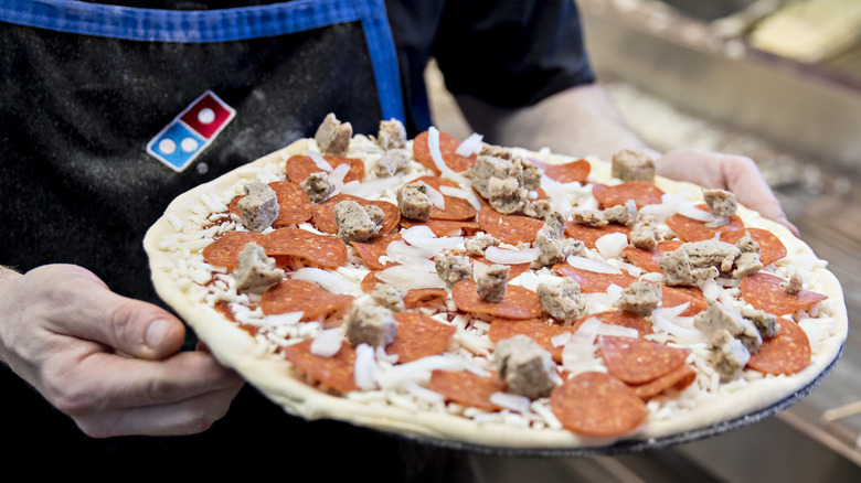 Employee making pizza with lots of toppings at Dominos