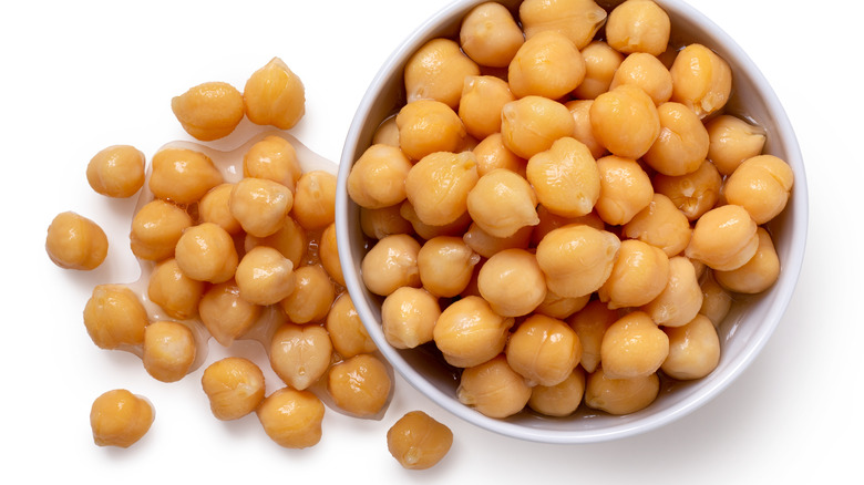 Cooked chickpeas in a white bowl, next to other wet chickpeas