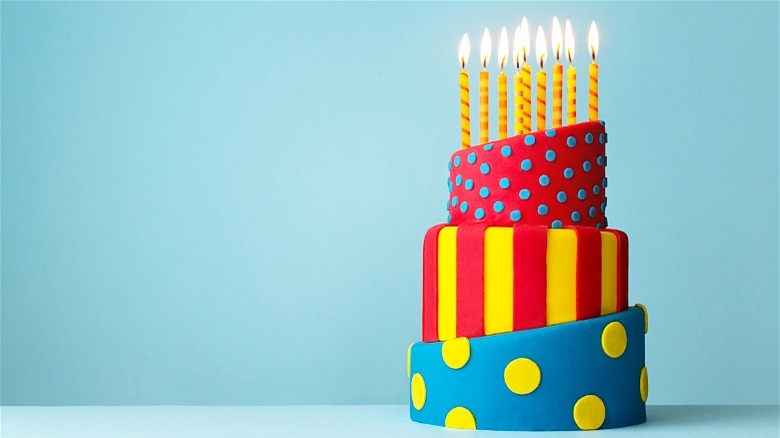 Multi-layered red, yellow, and blue cake with candles