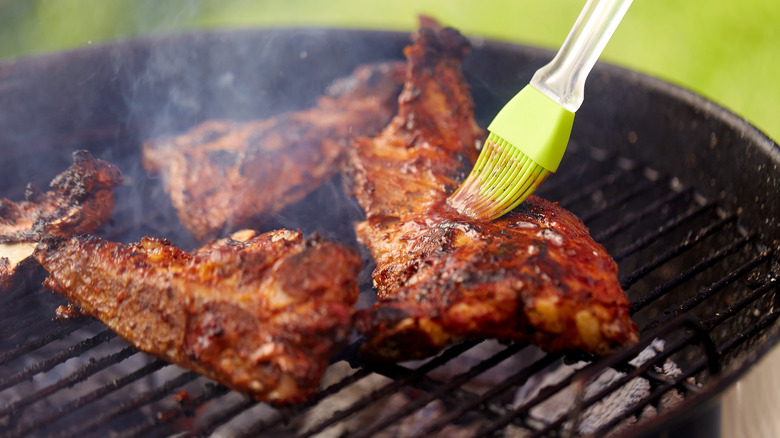 Chicken being brushed with sauce while on the grill