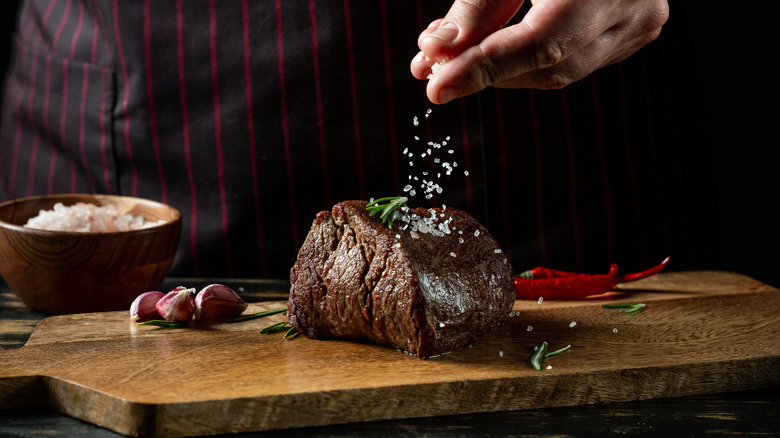 Chef salting a cooked steak on wood slab