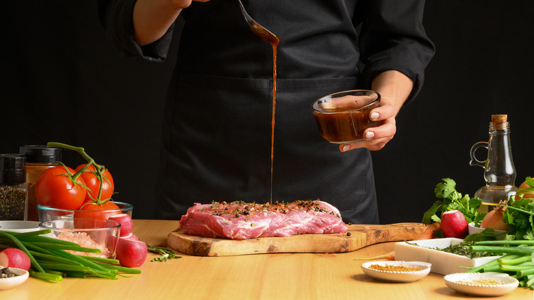 Chef pouring brown liquid marinade on raw meat