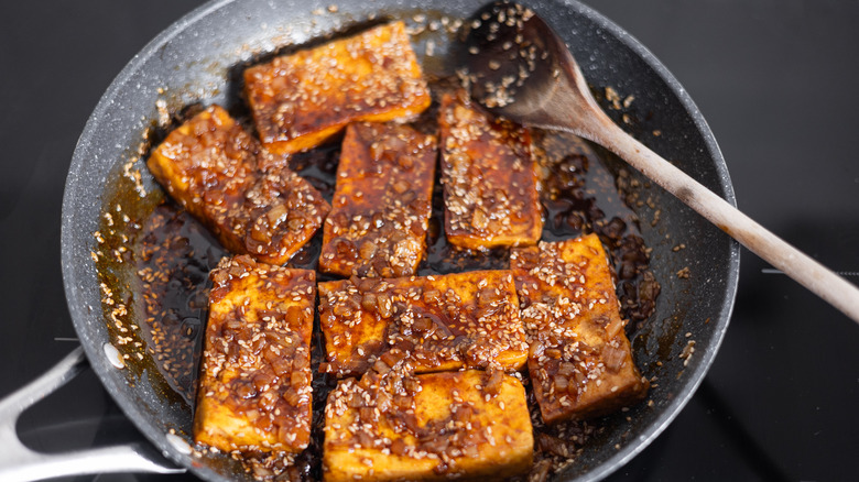 spooning sauce on tofu in pan