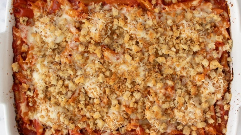 cooked pasta in tomato sauce in a white casserole dish topped with breadcrumbs