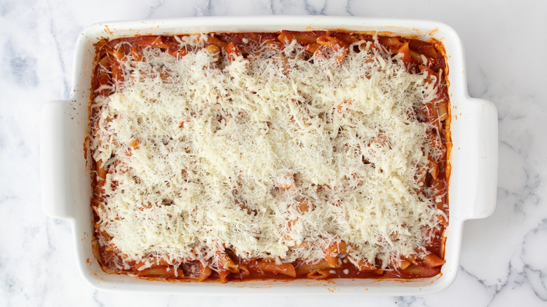 cooked pasta in tomato sauce in a white casserole dish topped with shredded cheese