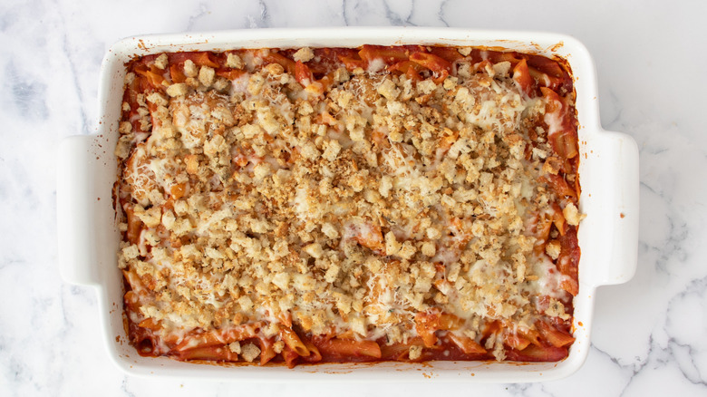 cooked pasta in tomato sauce in a white casserole dish topped with breadcrumbs