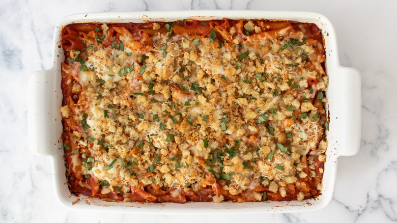 cooked pasta in tomato sauce in a white casserole dish topped with breadcrumbs and herbs