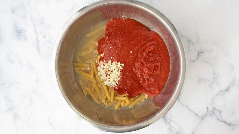 uncooked pasta and tomato sauce in a metal bowl with liquid