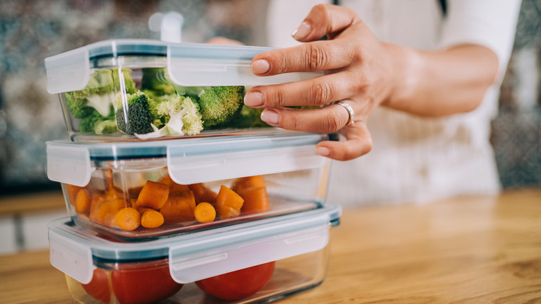 Person stacking three containers of vegetables 