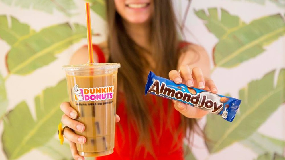 woman holding Dunkin' Donuts' iced coffee and Almond Joy candy bar