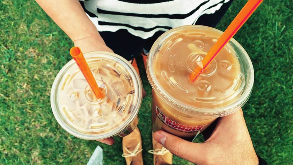 two people holding Dunkin' Donuts iced coffees