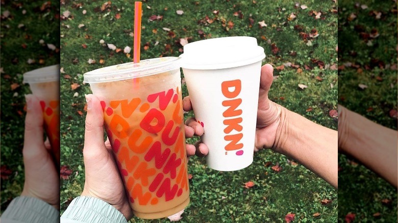Two people holding Dunkin' cups