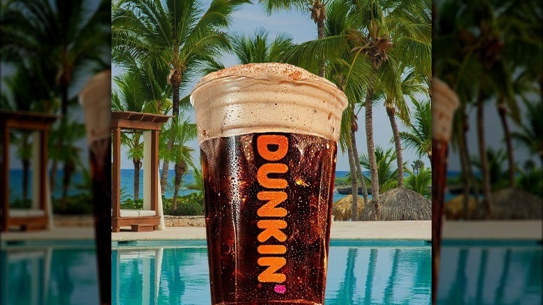Dunkin's new Brown Sugar Cream Cold Brew drink at a pool surrounded by palm trees.