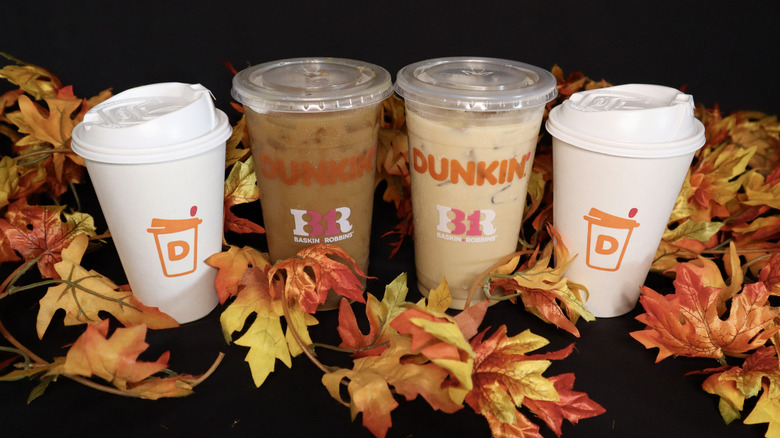 four Dunkin' drinks with fall leaves on black background