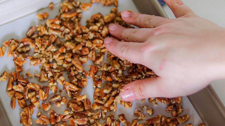 hand touching pecans in pan