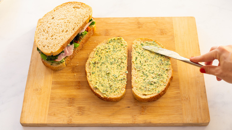 hand buttering sliced bread on wood cutting board