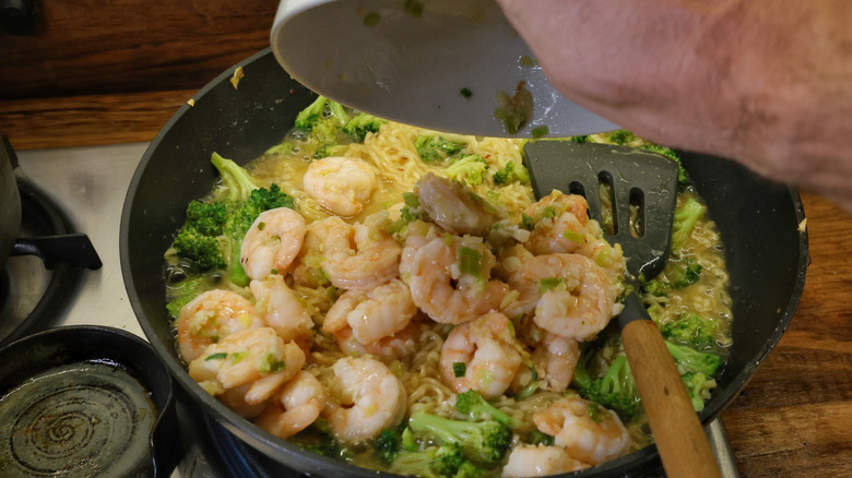 pouring bowl of cooked shrimp into skillet