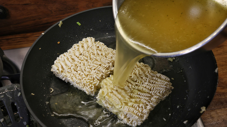 pouring broth over ramen noodles in skillet