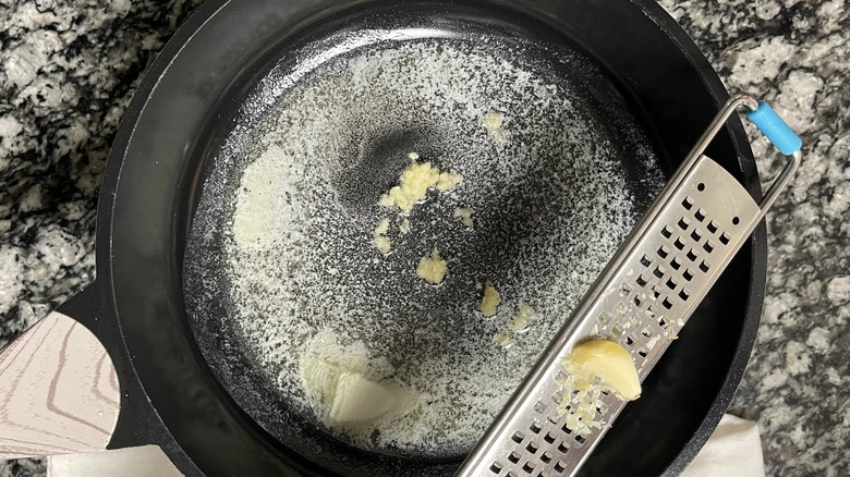 Garlic being grated into skillet with melted butter