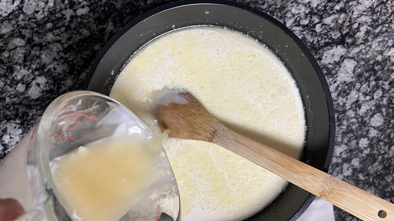 Stock pouring into skillet with cream and wooden spoon