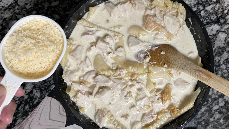 Parmesan cheese in measuring cup next to creamy lasagna skillet