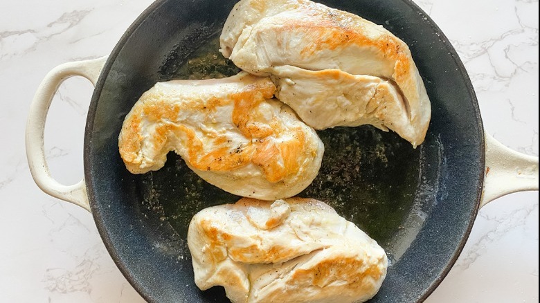 three chicken breasts searing in skillet