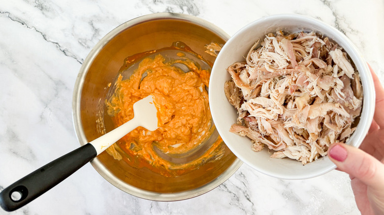 shredded chicken going into bowl with Buffalo sauce