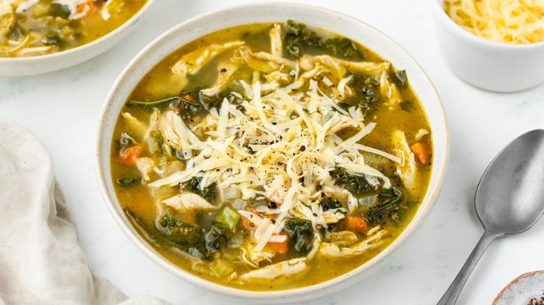 Chicken pesto soup in bowl with shredded cheese