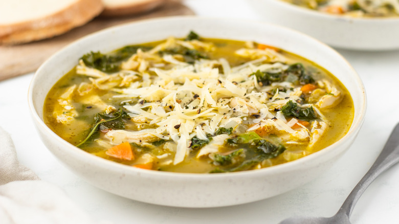 Chicken pesto soup in bowl with shredded cheese