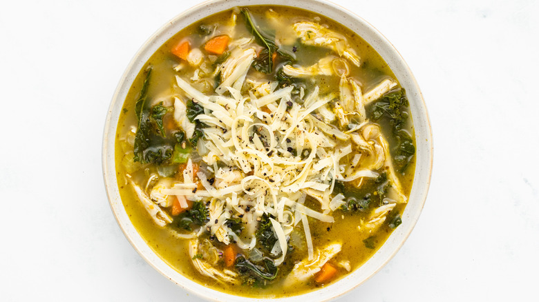 Chicken pesto soup in bowl with shredded cheese