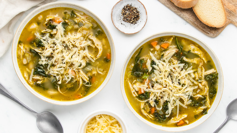 Two bowls of chicken pesto soup with shredded cheese