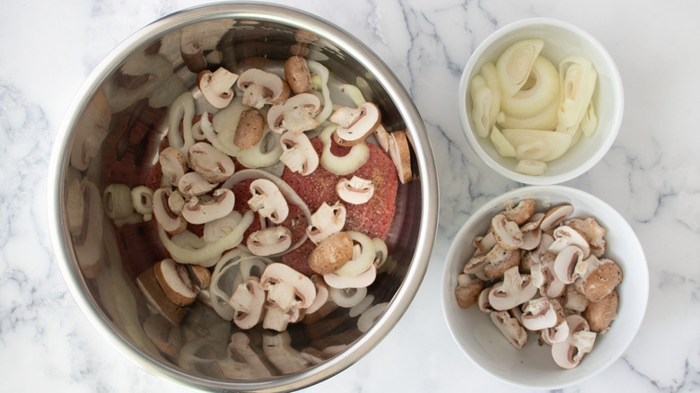 cubed steaks, mushrooms, and onions in a metal bowl