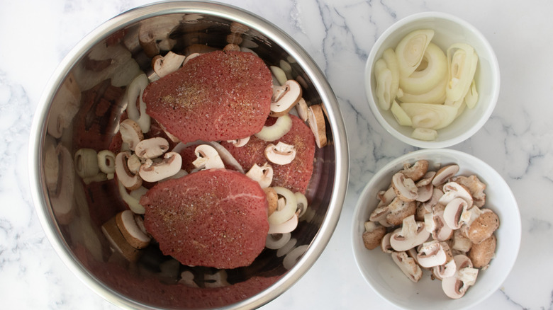 cubed steaks, mushrooms, and onions in a metal bowl