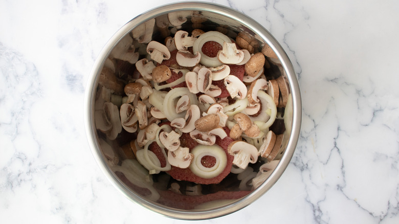 cubed steaks, mushrooms, and onions in a metal bowl