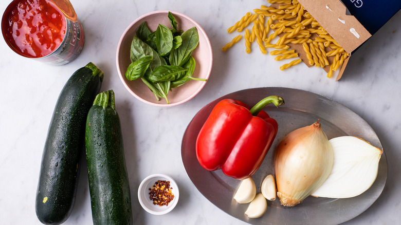 Ingredients gathered on a marble counter to make summer vegetable pasta.