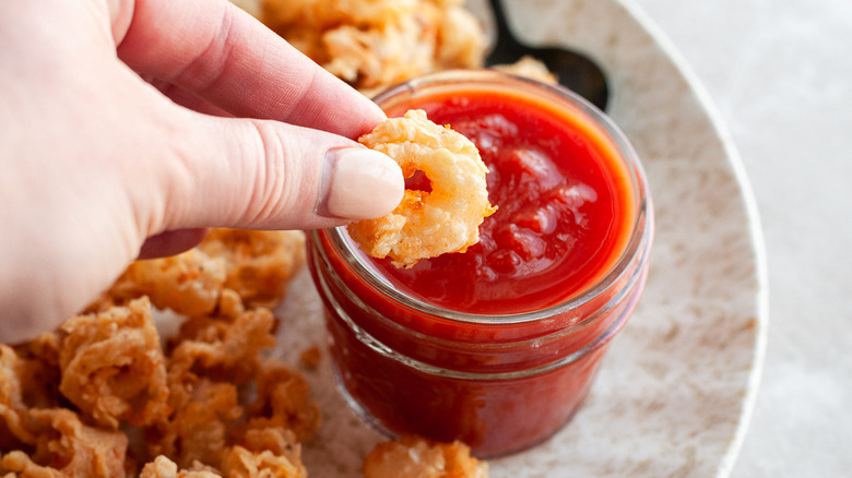 hand dipping fried calamari in sauce