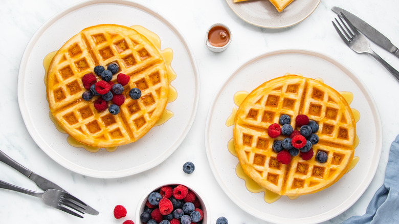 Waffles on two plates with berries and syrup