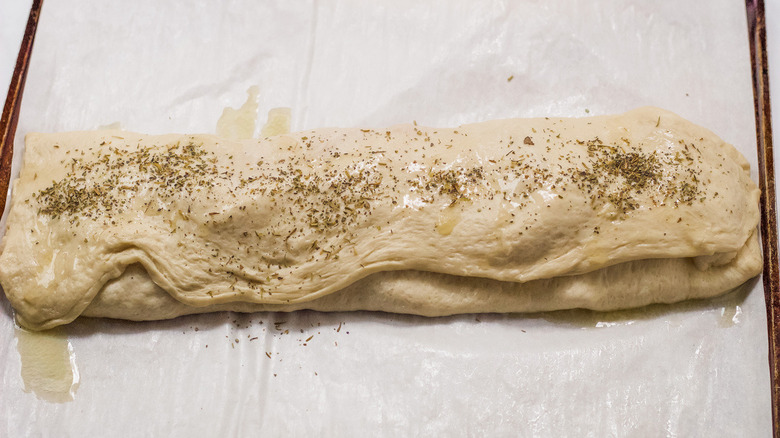 uncooked stromboli dough bathed in buttered and covered in Italian seasonings