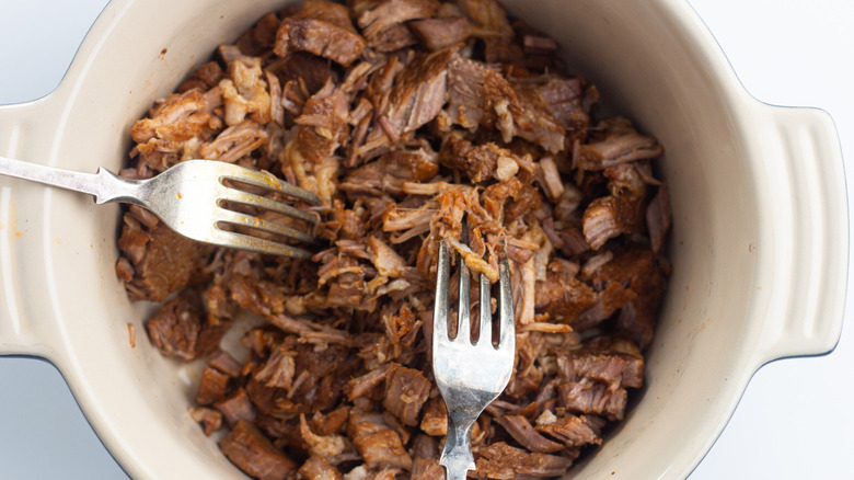 Two forks shredding pork in dish