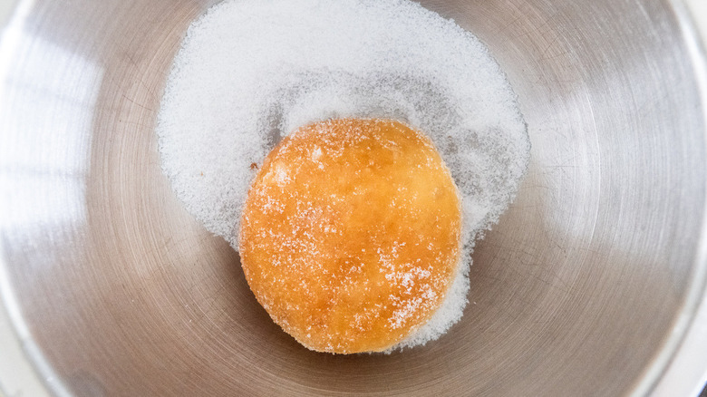 donut being rolled in granulated sugar in a metal bowl